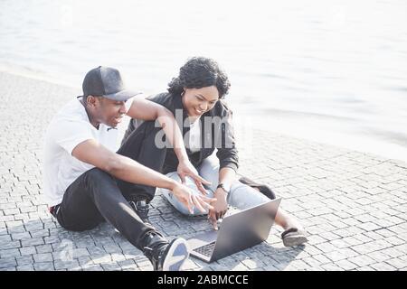 Deux amis heureux d'étudiants ou partenaires d'affaires sont assis à l'extérieur et bénéficiant d'un ordinateur portable Banque D'Images