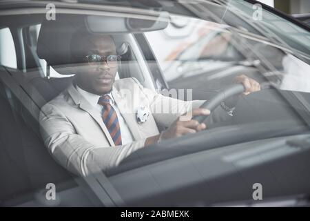 Vue avant du beau élégant africain des affaires sérieuses homme conduit une voiture Banque D'Images