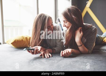 Deux soeurs jumelles cute smiling holding smartphone et décisions. selfies Les filles se coucher sur le canapé posant et la joie Banque D'Images