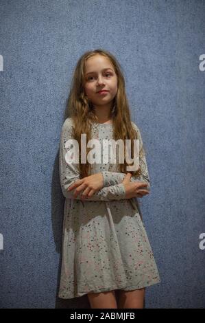 Fille de huit ans dans une robe en maille gris sur un fond bleu ou bleu mur à l'intérieur. Jolie fille 11 ans avec de longs cheveux blonds dans une gray d Banque D'Images