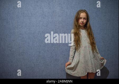 Fille de huit ans dans une robe en maille gris sur un fond bleu ou bleu mur à l'intérieur. Jolie fille 11 ans avec de longs cheveux blonds dans une gray d Banque D'Images