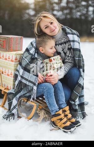 Heureuse mère et fils s'amusant avec traîneau dans une forêt d'hiver. Jour de neige d'hiver. Joli garçon avec sa maman sur un traîneau, serrant et souriante, tenant Banque D'Images