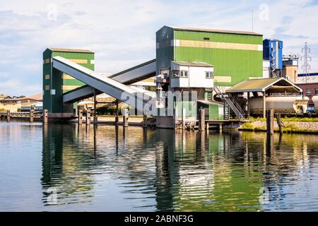 Chariot élévateur à grain avec système de chargement des barges et sur un canal dans le port fluvial de Strasbourg, France, avec un train de wagons-trémies sous attente. Banque D'Images