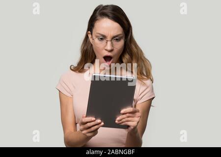 Choqué jeune femme portant des lunettes à la tablette à écran de l'ordinateur Banque D'Images