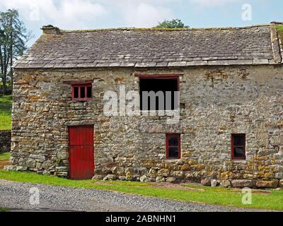 Vieille porte rouge dans l'ancienne grange de ferme en pierre traditionnelle dans la région de Eden Valley, Cumbria, England, UK Banque D'Images