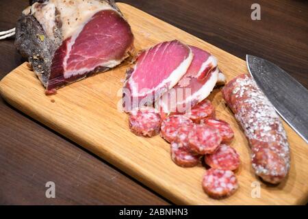 Tranches de jambon cru maison salé ou du prosciutto et des saucisses sur une planche en bois avec porte-couteau Banque D'Images