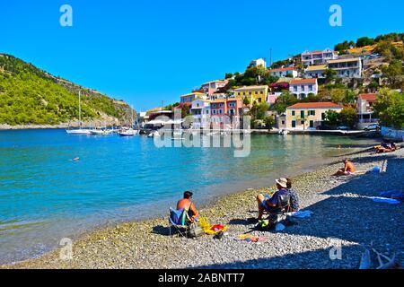 Assos, Kefalonia / Grèce - 9/13/2019 : une vue de la petite plage de galets dans le beau village de pêcheurs d'Assos.maisons colorées sur la colline. Banque D'Images