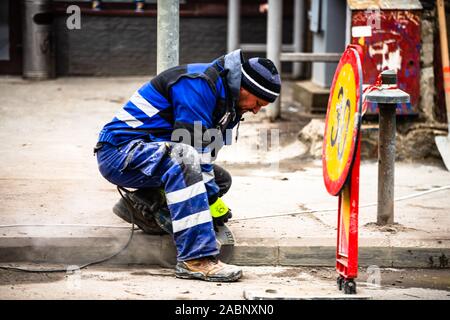 Travailleur de la construction d'asphalte pour pavage de coupe à l'aide d'un trottoir pour poignarde cut-off a vu, diamant lame de scie, machine à Bucarest, Roumanie, 2019 Banque D'Images