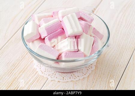 Blanc Rose fluffy les guimauves dans un bol en verre sur une table en bois. Hiver doux et savoureux de la nourriture. Close-up de délicieux bonbons mous. Vue de face. Banque D'Images