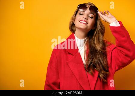 Une belle fille avec le rouge à lèvres rouge dans un manteau avec sa tête en arrière et souriant avec ses yeux fermés, soulevant des lunettes Banque D'Images