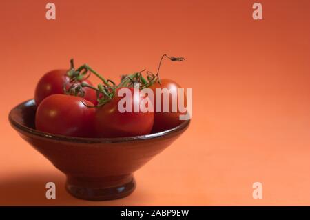Un bol brun avec quelques tomates cerises sur branch sur fond orange et de l'espace pour la copie des textes (l'espace) Banque D'Images