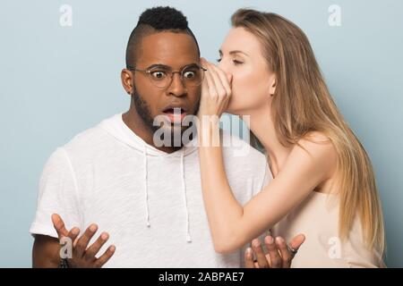 Woman Whispering in African American man ear, dire aux nouvelles inattendues Banque D'Images