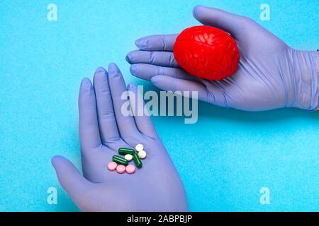 Cerveau rouge sur un fond bleu avec des pilules dans les mains d'un médecin. Certains médicaments pour le cerveau. C'est symbolique pour les médicaments, les psychotropes Banque D'Images