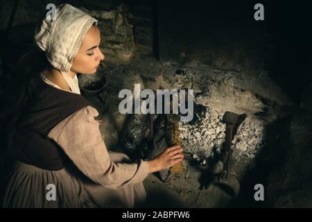 Portrait de la Renaissance dans le style de Rembrandt d'une jeune femme en costume paysan médiéval travaux près de la cheminée authentique d'un bien français parution Banque D'Images