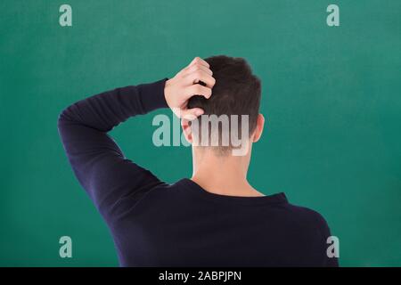 Vue arrière du jeune homme en tee-shirt bleu se gratte la tête contre le fond vert Banque D'Images