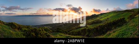 Vue panoramique d'un coucher du soleil sur les collines de Açores São Jorge campagne avec l'île de Pico dans la mer en arrière-plan avec le mont Pico's Summit. Banque D'Images