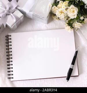 Album de mariage ou de l'écriture de livre sur la dentelle mariée avec plusieurs cadeaux de mariage d'argent et rose blanche bouquets. L'espace pour copier. Banque D'Images