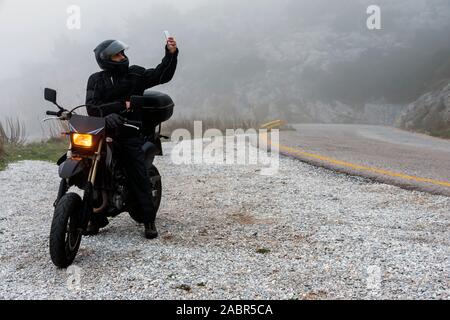 Rider tente de trouver de signal sur son mobile sur un jour brumeux monter sur les montagnes avec sa moto - projet ride aventure Banque D'Images