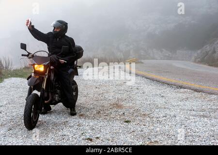 Rider tente de trouver de signal sur son mobile sur un jour brumeux monter sur les montagnes avec sa moto - projet ride aventure Banque D'Images