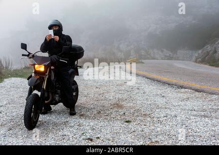 Rider tente de trouver de signal sur son mobile sur un jour brumeux monter sur les montagnes avec sa moto - projet ride aventure Banque D'Images