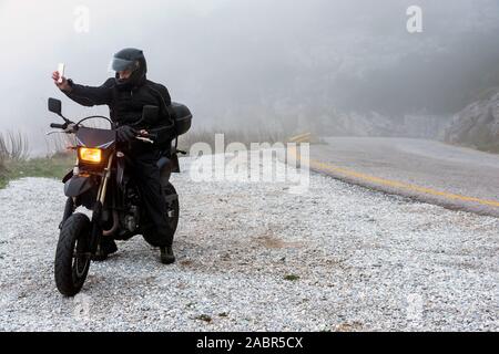 Rider tente de trouver de signal sur son mobile sur un jour brumeux monter sur les montagnes avec sa moto - projet ride aventure Banque D'Images