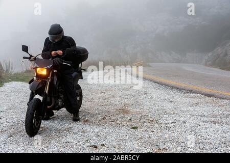 Rider tente de trouver de signal sur son mobile sur un jour brumeux monter sur les montagnes avec sa moto - projet ride aventure Banque D'Images