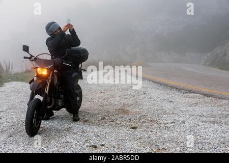 Rider tente de trouver de signal sur son mobile sur un jour brumeux monter sur les montagnes avec sa moto - projet ride aventure Banque D'Images