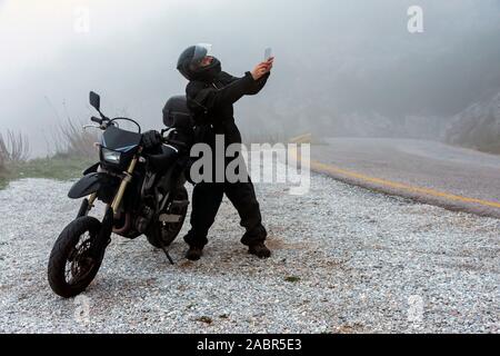 Rider tente de trouver de signal sur son mobile sur un jour brumeux monter sur les montagnes avec sa moto - projet ride aventure Banque D'Images