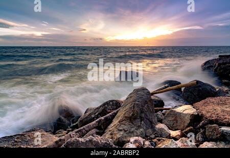 L'eau de l'océan des vagues sur la plage de rock avec beau coucher de soleil Ciel et nuages. Éclaboussures des vagues de la mer sur la pierre en mer sur la côte de l'été. Nature Paysage. Scieries Banque D'Images