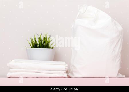 Close-up d'une pile de linge blanc, sac d'entreposage, de plante sur une table contre le mur de la lumière d'arrière-plan. Banque D'Images