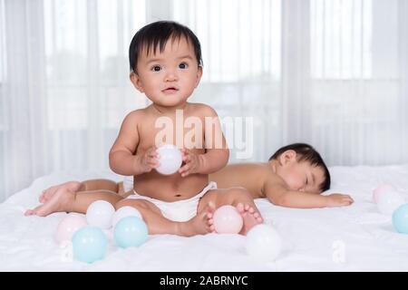 Lits bébés sur un lit, l'un jouant boule de couleur, 1 Banque D'Images