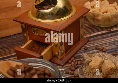Cuillère en bois dans un bocal de verre avec des grains de café, moulin à café, morceaux de sucre brun sur un fond de bois. Close up Banque D'Images