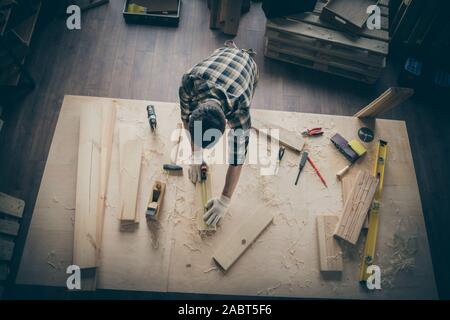 Haut haut au-dessus de l'homme view photo angle mesurant la longueur de morceau en bois en chemise à carreaux entouré d'instruments à l'intérieur Banque D'Images