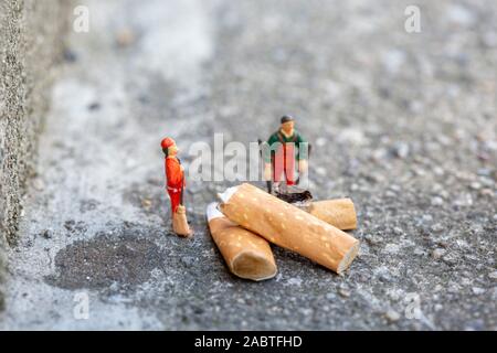 Deux poubelles miniatures nettoient et balaient des cigarettes fumées dans la rue qui polluent l'environnement Banque D'Images