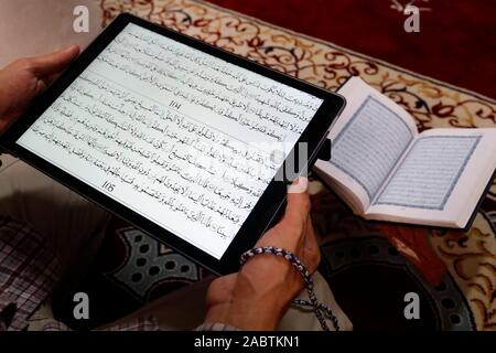 Une lecture musulmane Coran numérique sur une tablette.en arrière-plan un document papier traditionnel arabe Saint Coran. Banque D'Images