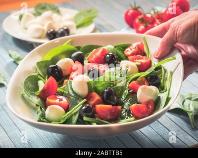 Mains courantes salade d'épinards, légumes, aliments sains avec tomates, mozzarella, olives noires. vue rapprochée Banque D'Images