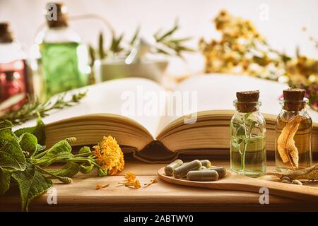 La médecine traditionnelle pour la préparation de médicaments avec capsules et de guérison des essences et des livre sur table en bois. Vue de face. Compo horizontale Banque D'Images