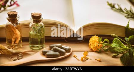 La médecine traditionnelle pour la préparation de médicaments avec capsules et de guérison des essences et des livre sur table en bois. Vue de face. Vue panoramique compos Banque D'Images