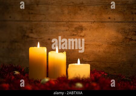 La chaleur de la notion de Noël : trois chandelles allumées sur une table en bois clair et un cadre rustique avec des branches de pins, décoration rouge et or et re Banque D'Images