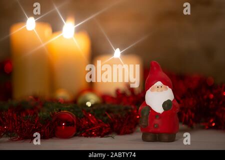 La chaleur de la notion de Noël : un Père Noël, statuette en premier plan dans un cadre rustique avec des bougies allumées en trois avec effet de flou, d'or et r Banque D'Images