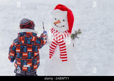 Kiev. L'Ukraine. 01.10.2016. Cute little boy fait sourire et tire sur le visage bonhomme dans Winter Park. enfant jouant avec la neige. Kid sculpte gros bonhomme de neige. Chil Banque D'Images