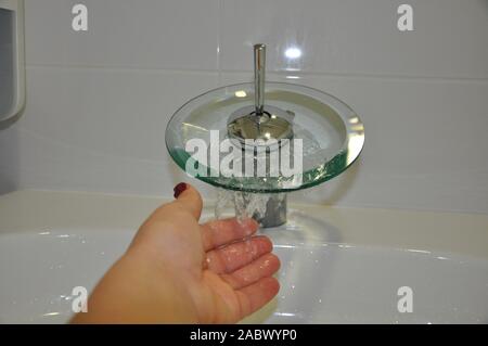 Femme se lavant les mains sous l'eau courante.un robinet en verre moderne d'où l'eau coule Banque D'Images