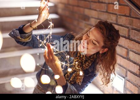 Heureux redhead Caucasian woman Playing with fairy lights outdoors Banque D'Images