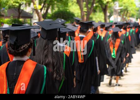 Vue arrière du groupe de diplômés universitaires en robes noires s'aligne pour le diplôme à l'université cérémonie de remise de diplômes. L'éducation Concept félicitations, stu Banque D'Images