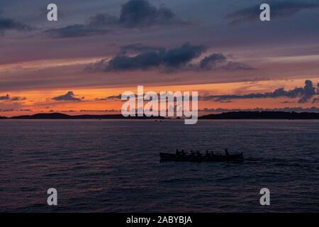 Un bateau pilote Cornish gig étant ramé entre les îles Scilly au coucher du soleil Banque D'Images