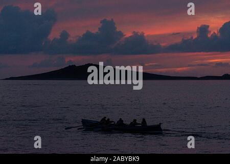 Un bateau pilote Cornish gig étant ramé entre les îles Scilly au coucher du soleil Banque D'Images