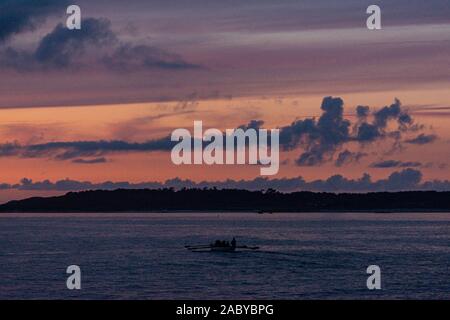 Un bateau pilote Cornish gig étant ramé entre les îles Scilly au coucher du soleil Banque D'Images