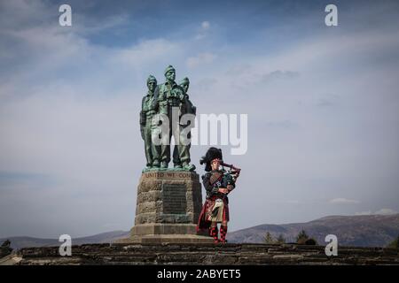 Un joueur de cornemuse joue en face de la statue commémorative de commando de la DEUXIÈME GUERRE MONDIALE à Spean Bridge, commandée en 1949 par le sculpteur Scott Sutherland. Banque D'Images