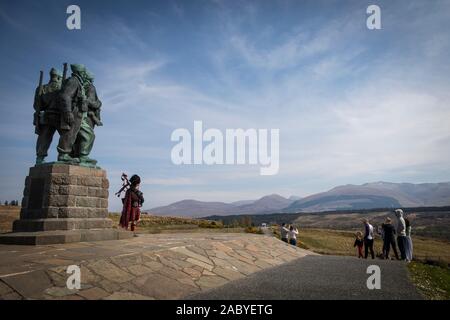 Un joueur de cornemuse joue en face de la statue commémorative de commando de la DEUXIÈME GUERRE MONDIALE à Spean Bridge, commandée en 1949 par le sculpteur Scott Sutherland. Banque D'Images