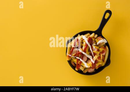 Salchipapa typique de l'Amérique latine. Les saucisses avec des frites, du ketchup, de la moutarde et la Mayo dans poêle de fer et fond jaune Banque D'Images